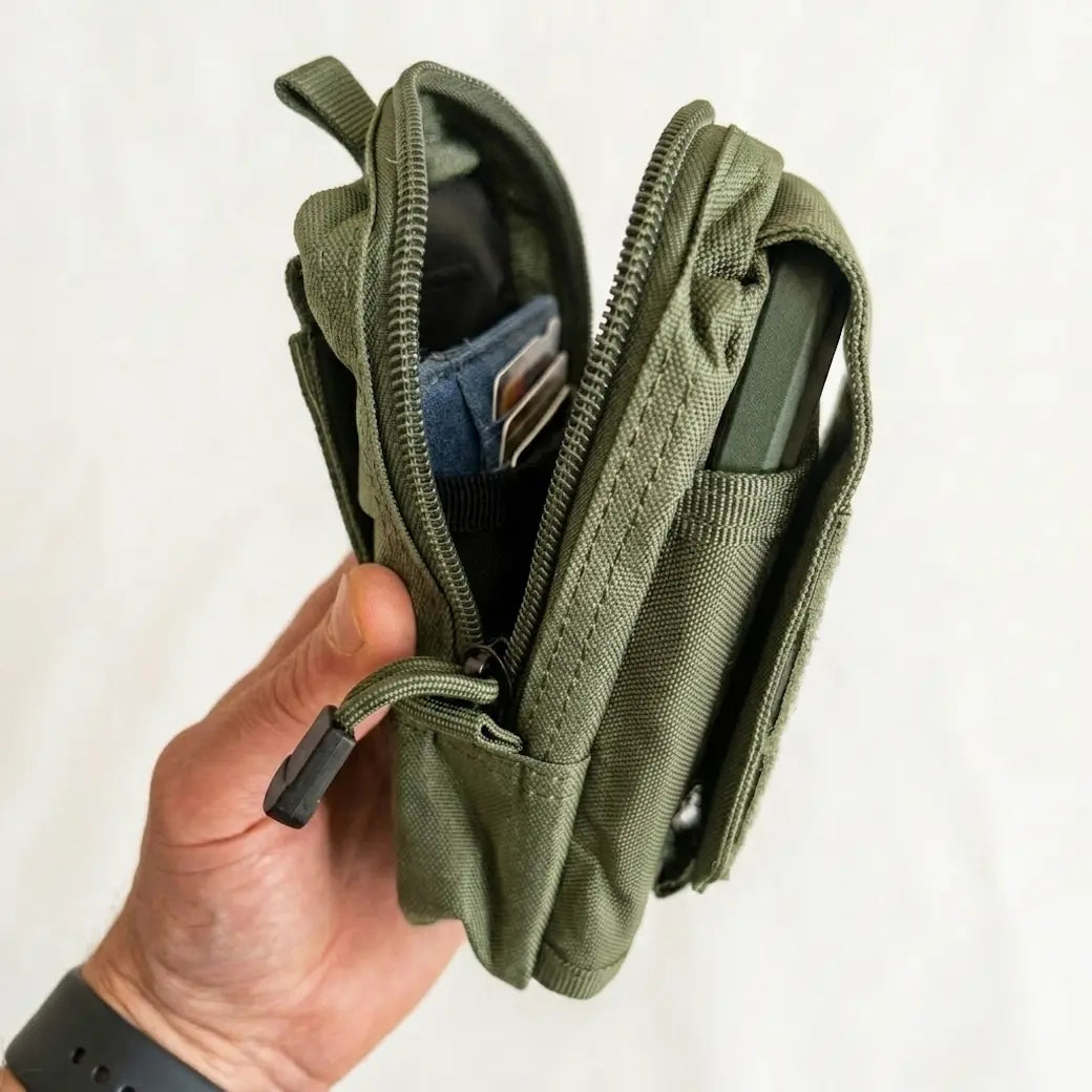 An olive green tactical pouch wallet being held open by a hand, showing its interior compartments, zipper, and card slots against a plain white background.