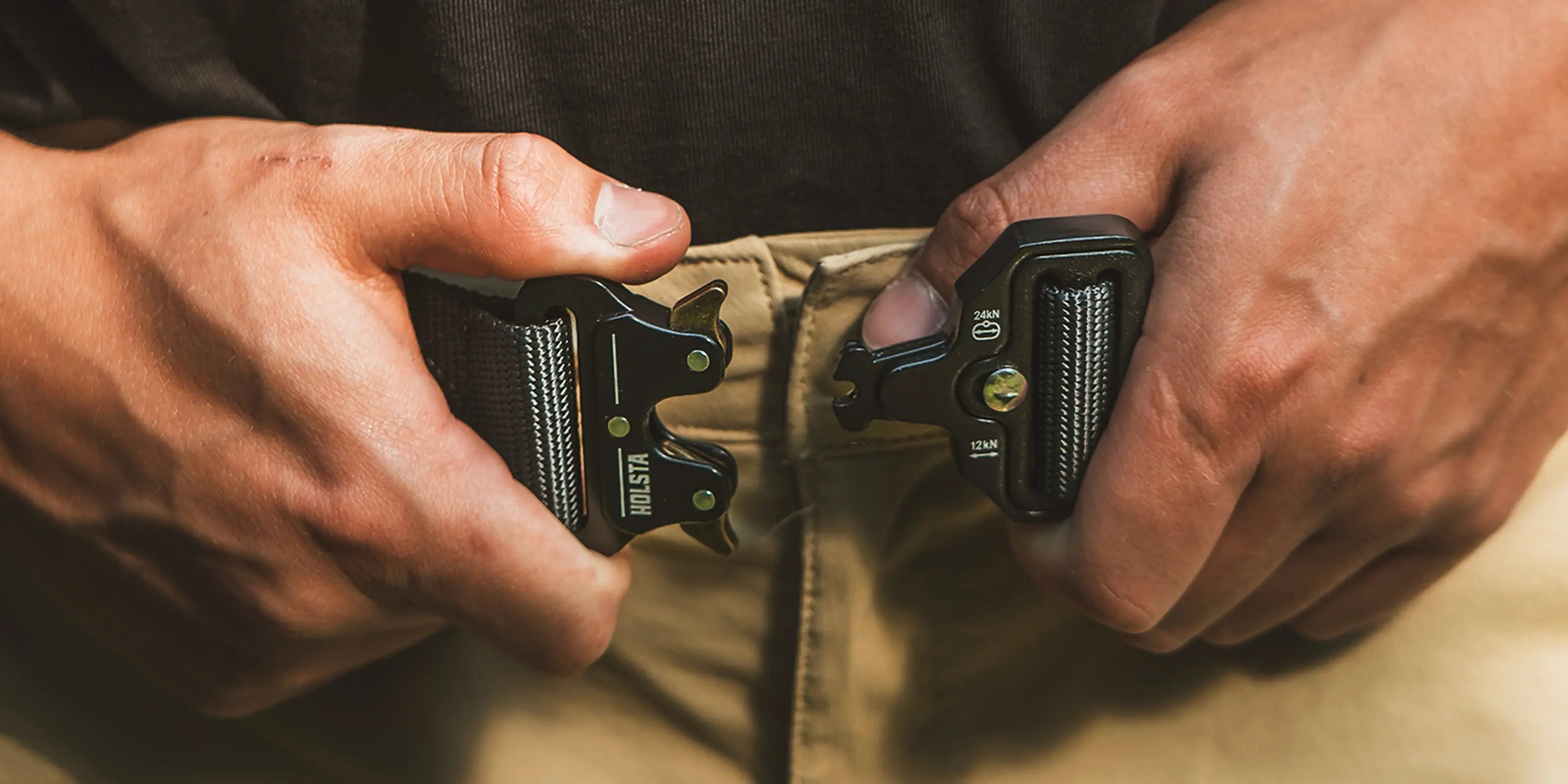 Hands doing up unbuckled black Holsta Belt around waist of man wearing beige trousers and black top