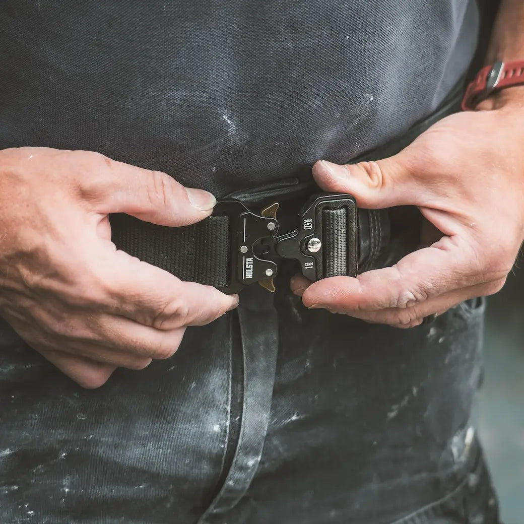 Close-up of a person's hands adjusting a black adjustable work belt with a quick-release metal buckle over dark clothing.